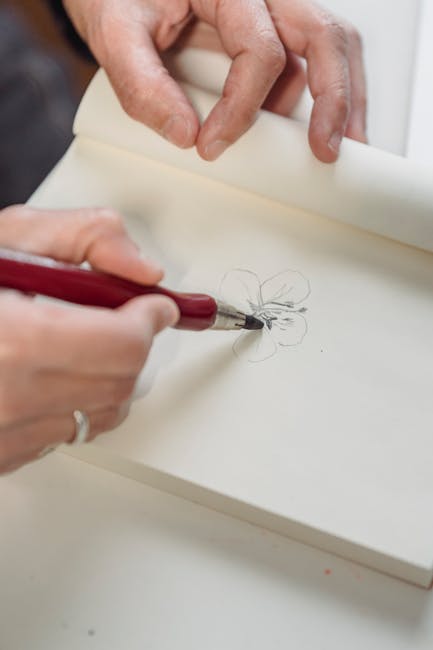 Person sketching a flower in a blank notebook with a pencil.