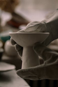 Gloved hands sculpting a ceramic piece in an artistic pottery workshop, showcasing craftsmanship.